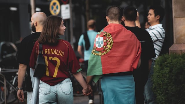 A group of football fans in Berlin, one wearing a Portugal flag, walking the street.