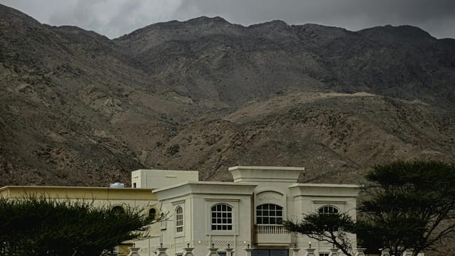 A luxurious villa set against the rugged mountains of Fujairah, UAE, under cloudy skies.