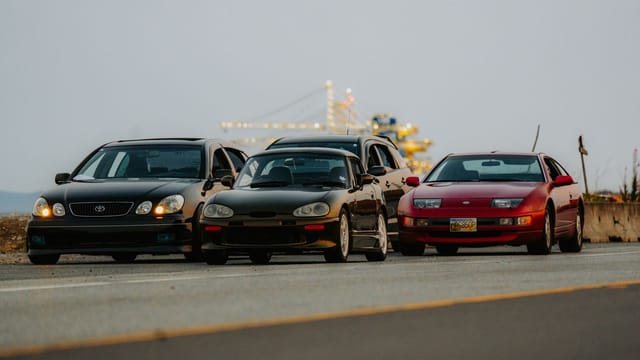 Four classic sports cars line up on a scenic road, ready for adventure.