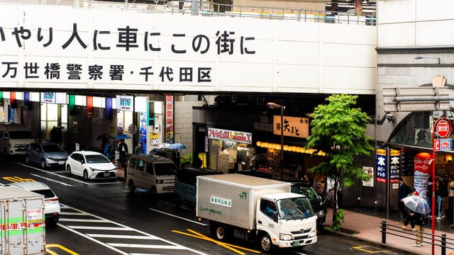 Bustling street view in Tokyo, Japan, with colorful umbrellas and vehicles during a rainy day.