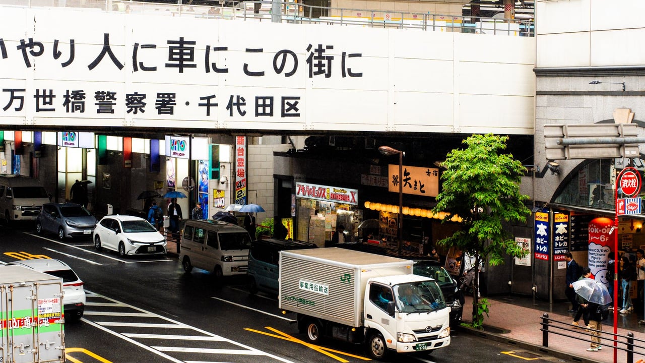 Bustling street view in Tokyo, Japan, with colorful umbrellas and vehicles during a rainy day.