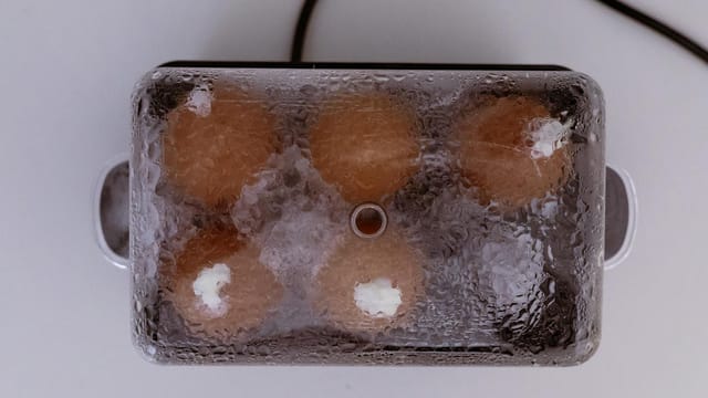 Top view of eggs being cooked in an electric egg steamer with mist on lid.