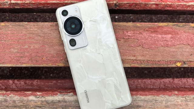 Modern smartphone with a textured back cover lies on a rustic wooden bench outdoors.