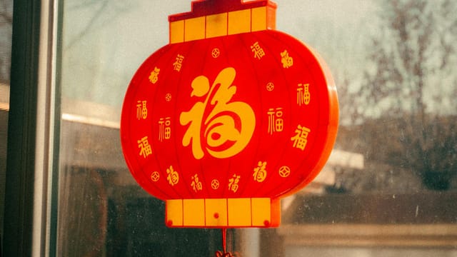 Red Chinese lantern with golden characters hanging near a window, symbolizing prosperity and celebration.