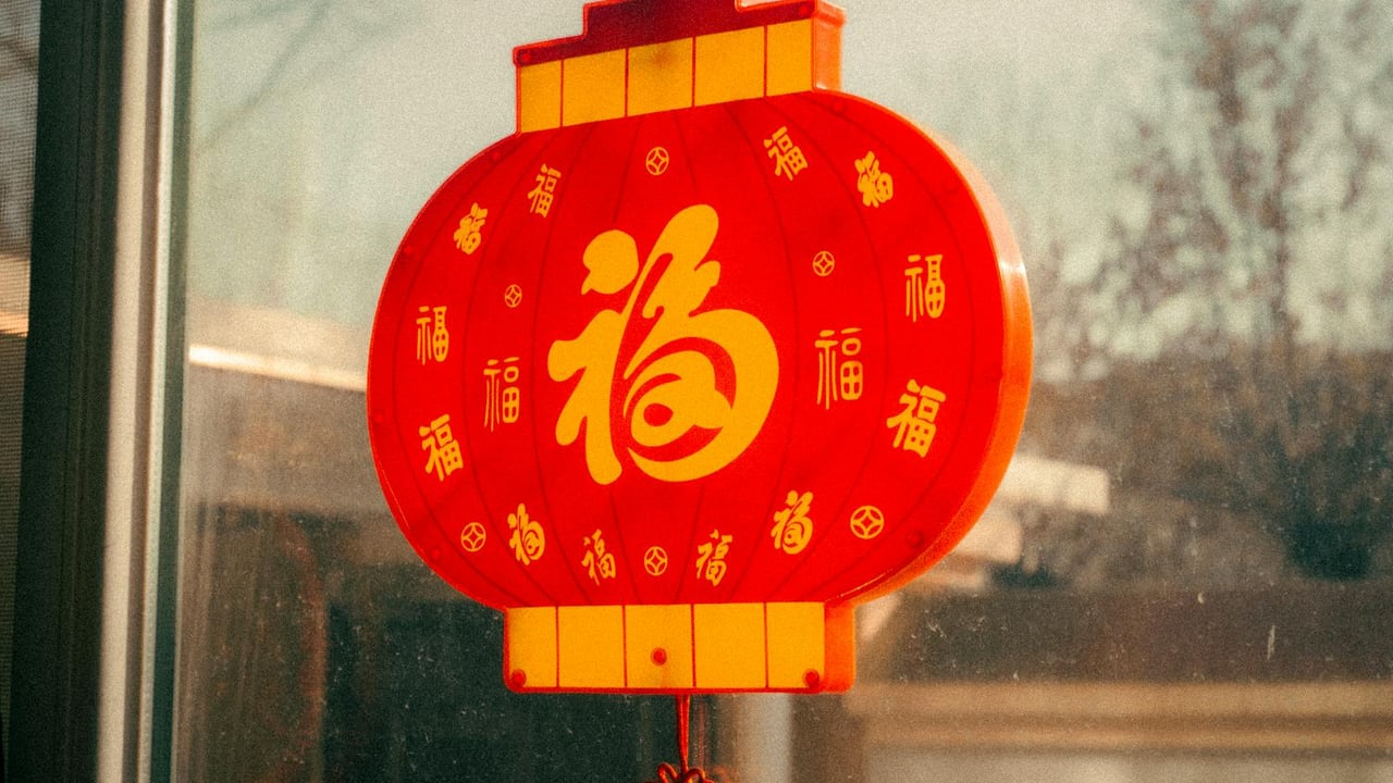 Red Chinese lantern with golden characters hanging near a window, symbolizing prosperity and celebration.