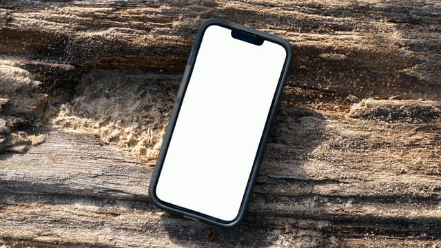 iPhone mockup with blank screen on a sandy wooden log at Kamala Beach, Phuket, Thailand.