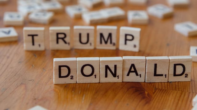 Close-up of Scrabble tiles spelling 'Donald Trump' on a wooden table.