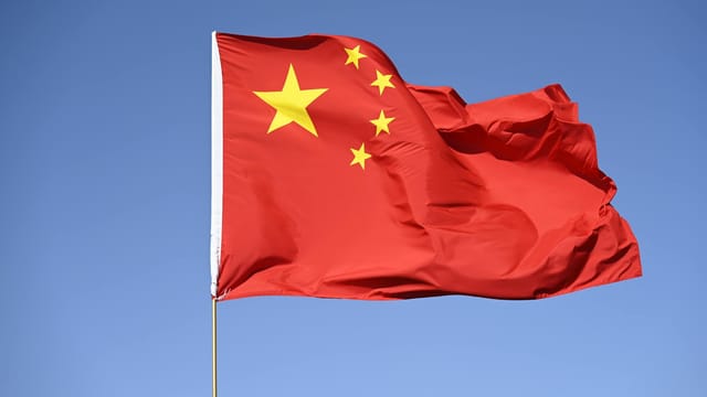 Chinese national flag flying high against a clear blue sky, symbolizing unity and pride.