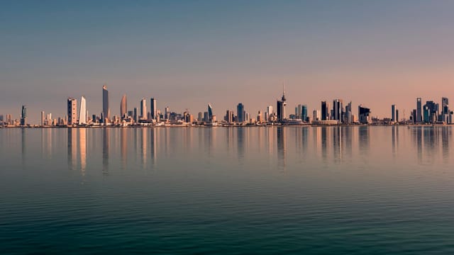 Beautiful Kuwait City skyline reflected on calm water at sunset, showcasing modern architecture.