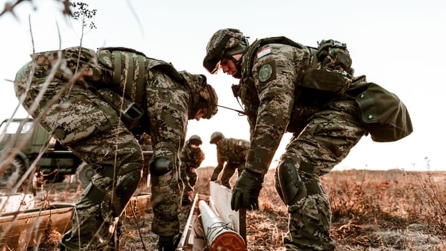 Soldiers in camouflage uniforms during training exercises at sunset in an open field.
