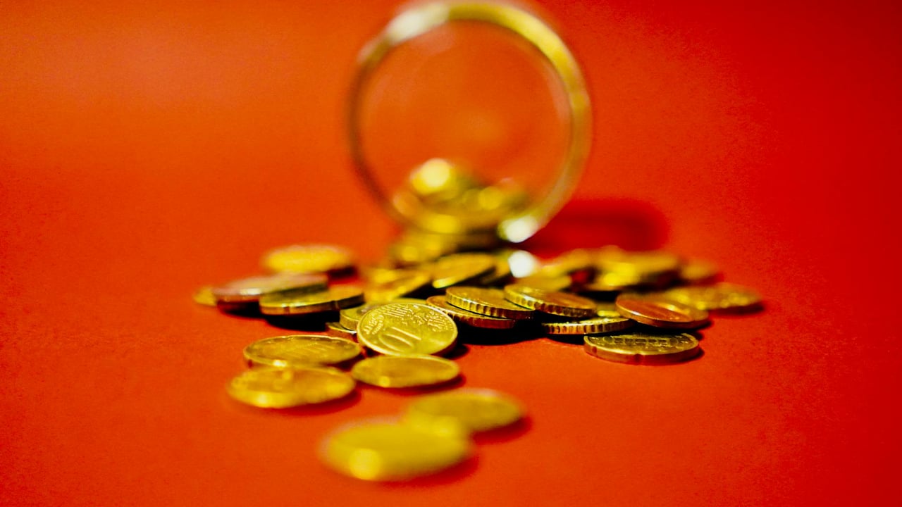 A collection of golden coins spilling from a glass jar on a vibrant red background symbolizes wealth.