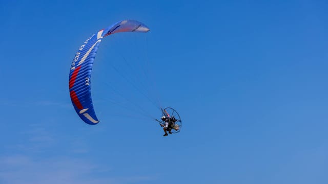 A person flies a paramotor under a clear blue sky in Sam Roi Yot, Thailand.