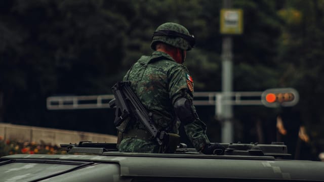 A soldier in camouflage uniform stands on a military vehicle in Mexico City, CDMX.