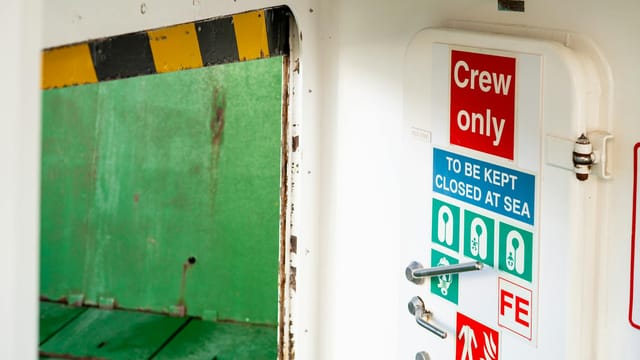 A crew-only door sign with maritime safety symbols on a ferry in Scotland.