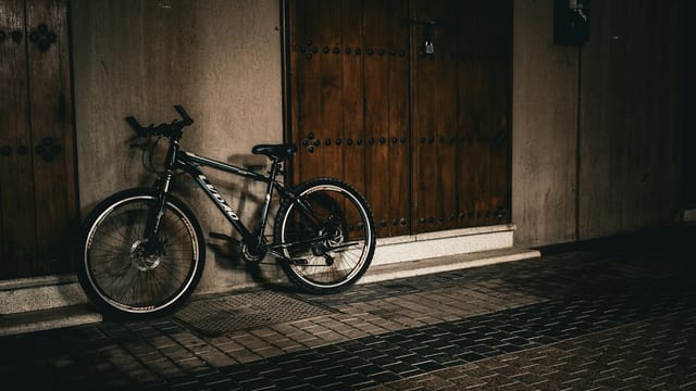 A bicycle parked against traditional wooden doors on an urban street in Kuwait.
