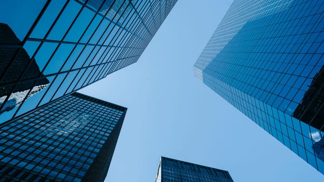From below of contemporary high rise buildings with glass walls located on street with sunlight in modern district of city