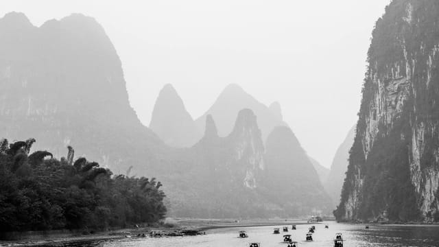 Black and white view of the Li River with boats and karst mountains in Guilin, China.