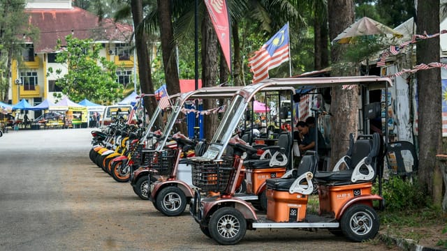 Electric scooters and motorcycles are parked along a market street in Malaysia.