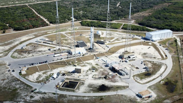 Drone view of spaceport with installed rocket ready for launching steel towers and hangar located amidst green forest
