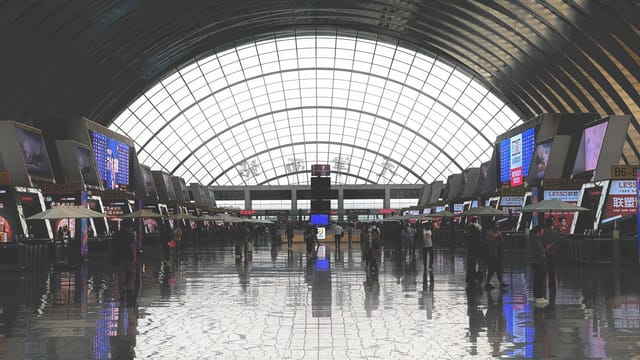 Wide view of the Tianjin railway station lobby with people bustling under the arched roof.