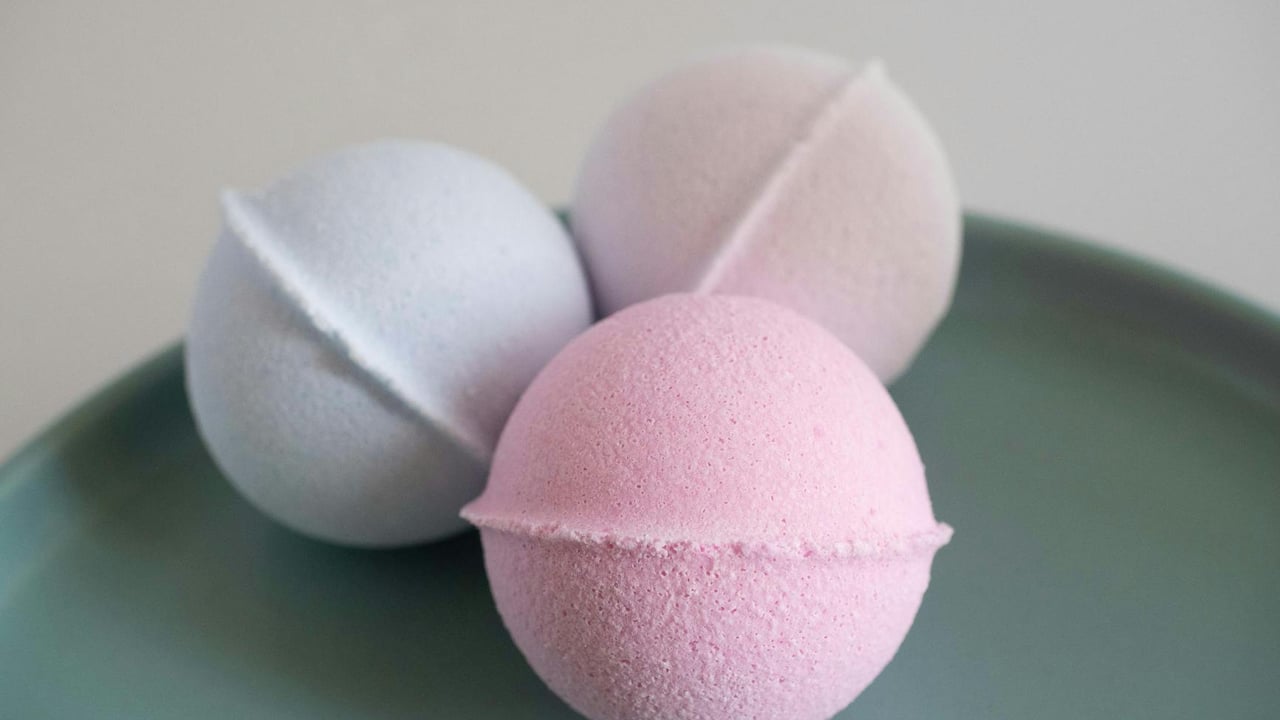 Three vibrant bath bombs displayed on a green ceramic plate, perfect for a spa setting.