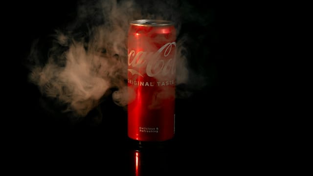 Red soda can with mist, captured on black background, perfect for refreshment concepts.