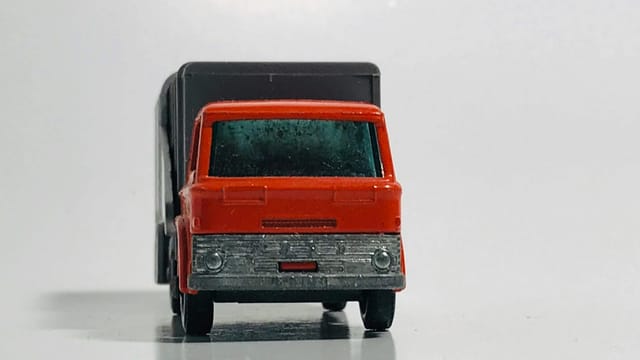 Front view close-up of a miniature red toy truck on a reflective white surface, emphasizing its details.