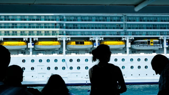 Silhouettes of people observing a large cruise ship from a dock in Türkiye.