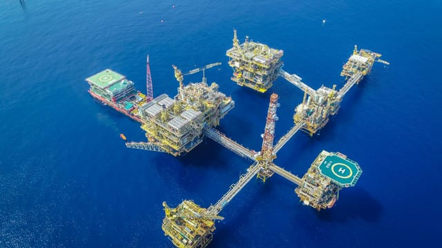 Drone shot of a large, complex offshore oil platform in deep blue ocean waters.
