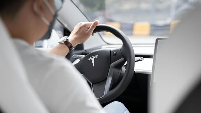 Close-up photo of a person driving a Tesla, showcasing modern vehicle interior design.