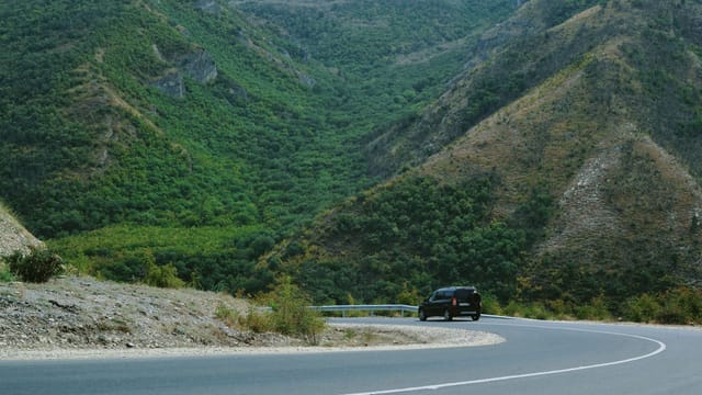 Illustrative image: A black car navigating a winding road through lush green mountains, perfect for travel themes.