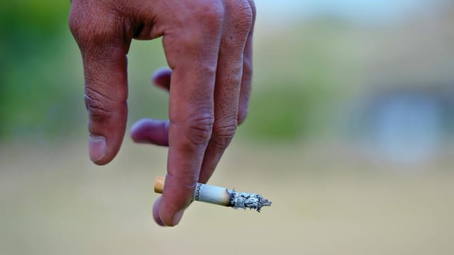 Detailed image of a hand holding a cigarette, signifying smoking habits and health risks.