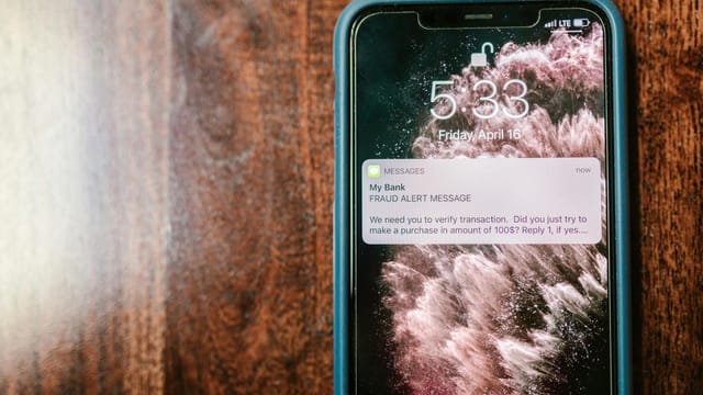 Close-up of a smartphone displaying a fraud alert notification on a wooden surface.