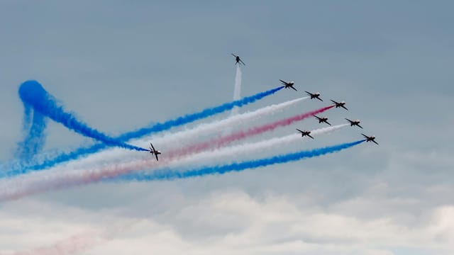 Aerobatic jets perform with vibrant smoke trails against a cloudy sky.