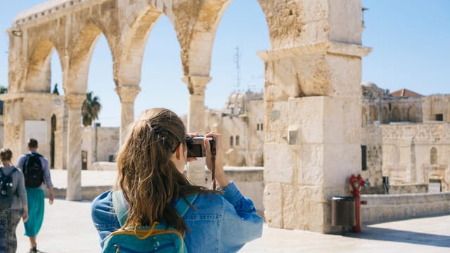 A tourist photographs the ancient stone arches in Jerusalem's Old Town, capturing the essence of travel and history.