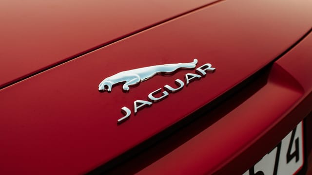 Detailed shot of Jaguar emblem on a red vehicle hood, emphasizing luxury.