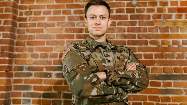 US Army soldier standing confidently with arms crossed against a brick wall, embodying pride and honor.