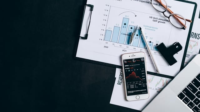 Top view of financial reports, smartphone showing stock market data, and a laptop on desk.