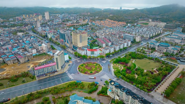 A vibrant aerial view of Jiujiang city showing buildings, roads, and greenery.