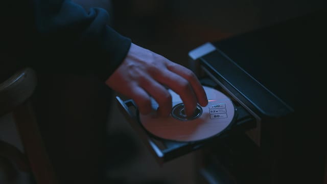 A hand inserting a CD into a computer drive, highlighting cyber security themes.