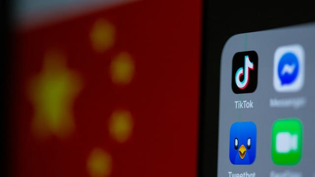 Close-up of a smartphone with popular social media app icons and blurred Chinese flag background.