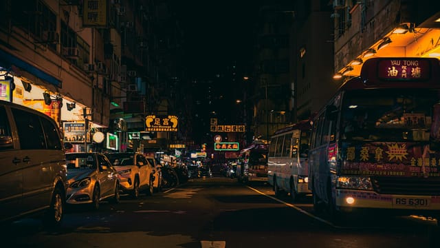 Bustling Hong Kong street nightlife with neon signs and busy traffic under dark skies.