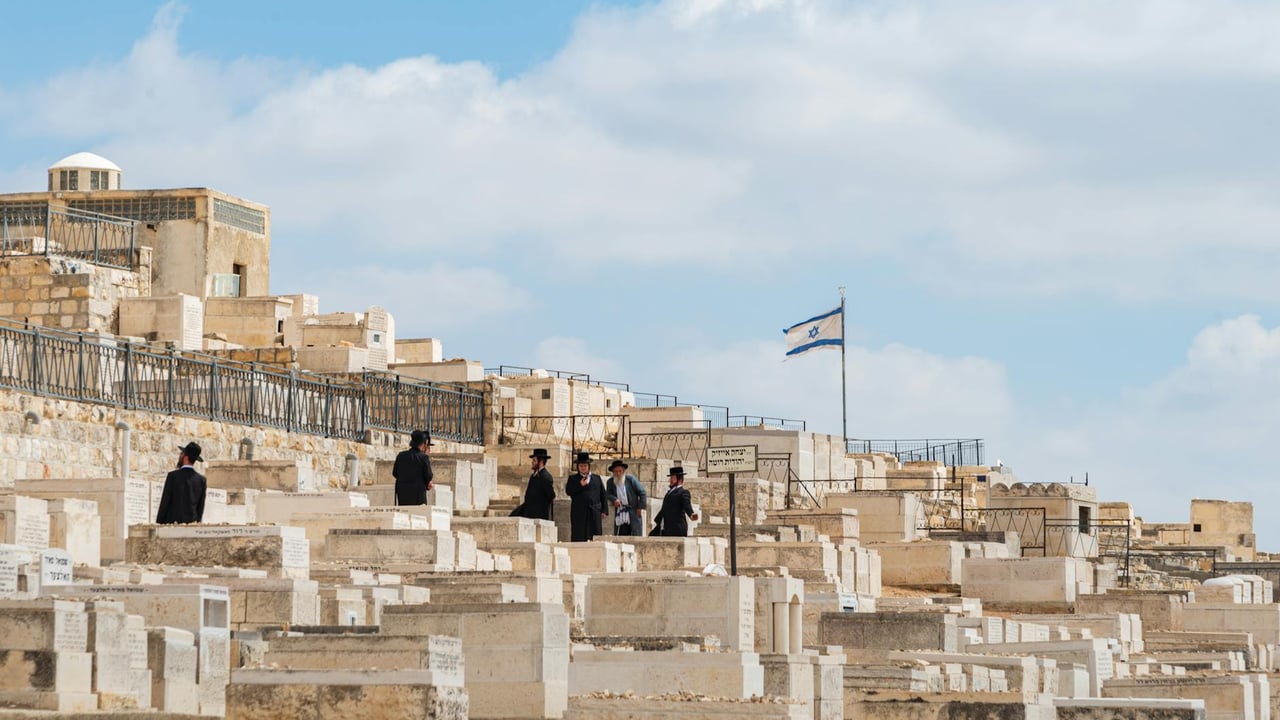 Orthodox Jewish men gather at Mount of Olives Cemetery in Jerusalem, Israel, under a clear sky.