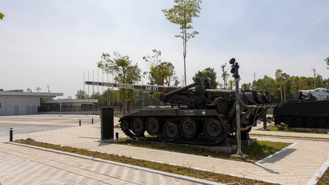 A historic military tank displayed outdoors in a sunny park setting.