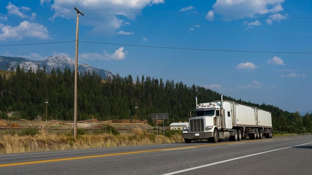 A white semi-truck traveling on a scenic road in Jaffray, BC, with mountains in the background.