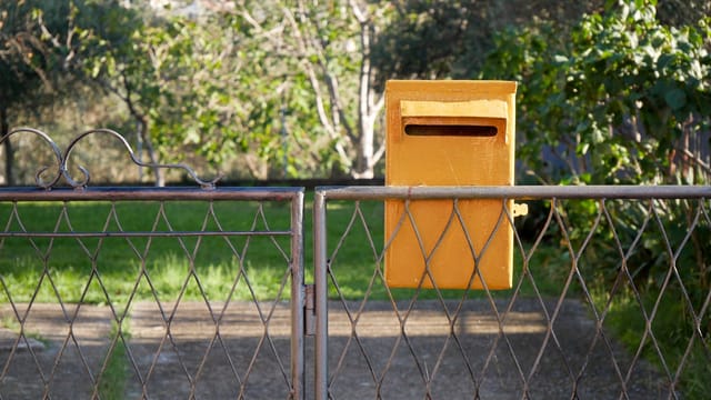A yellow mailbox attached to a metal gate in a lush green garden setting, perfect for stock use.