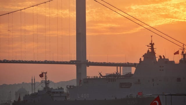 Military ships passing under a bridge in Istanbul during a stunning sunset on Bosporus Strait.