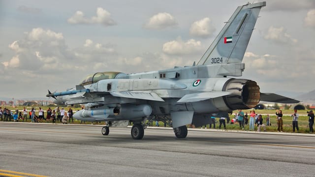 UAE Air Force F-16 jet on display at airshow with crowd watching.