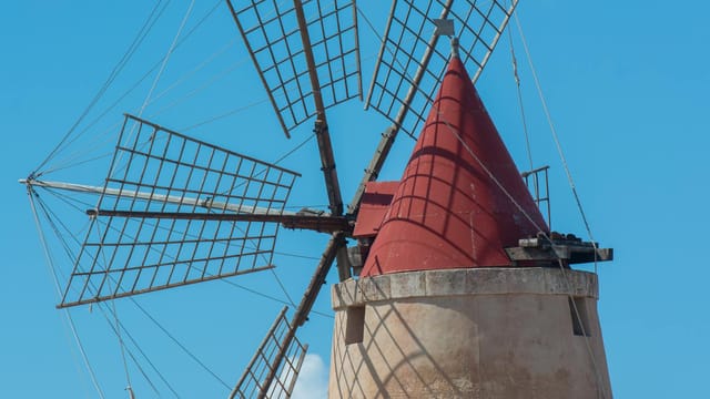 Traditional windmill with a red conical roof in Nubia, Sicily, Italy against a clear blue sky.