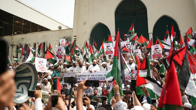 Large Pro-Palestinian demonstration in Dhaka with flags and banners supporting freedom and solidarity.